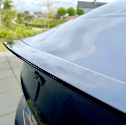 Blank sort ABS-spoiler monteret på bagklappen af en sort Tesla Model 3, set bagfra udendørs