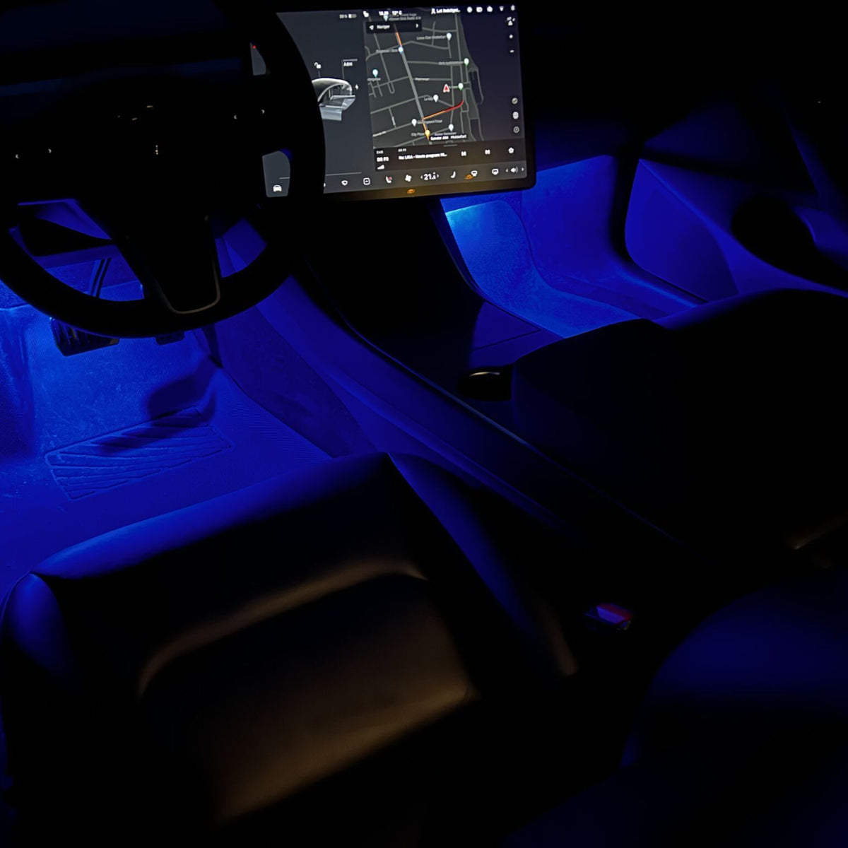 Tesla-kabine i mørke med blåt LED-ambientlys i fodrummene og infoskærmen tændt