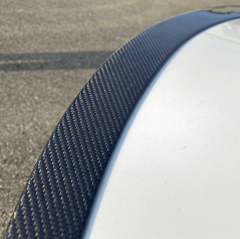 Nærbillede af carbon-spoilerens vævede kulfiber-struktur monteret på bagklappen af en hvid Tesla
