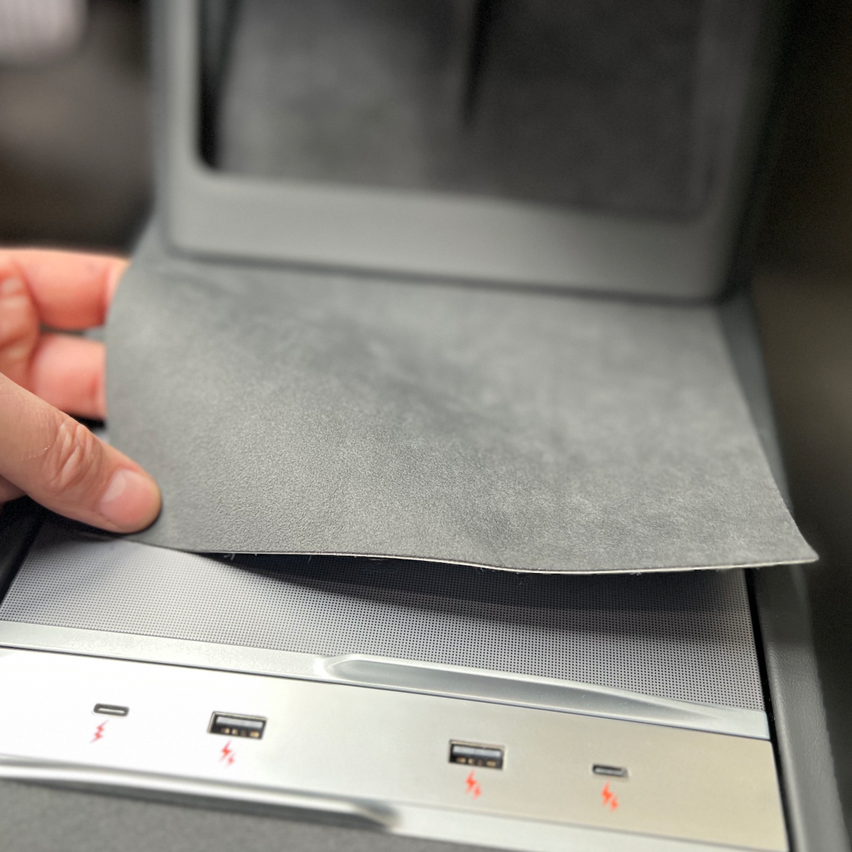En hånd der løfter folie-coveret af centerkonsollen i Tesla Model 3/Y og afslører USB-portene nedenunder