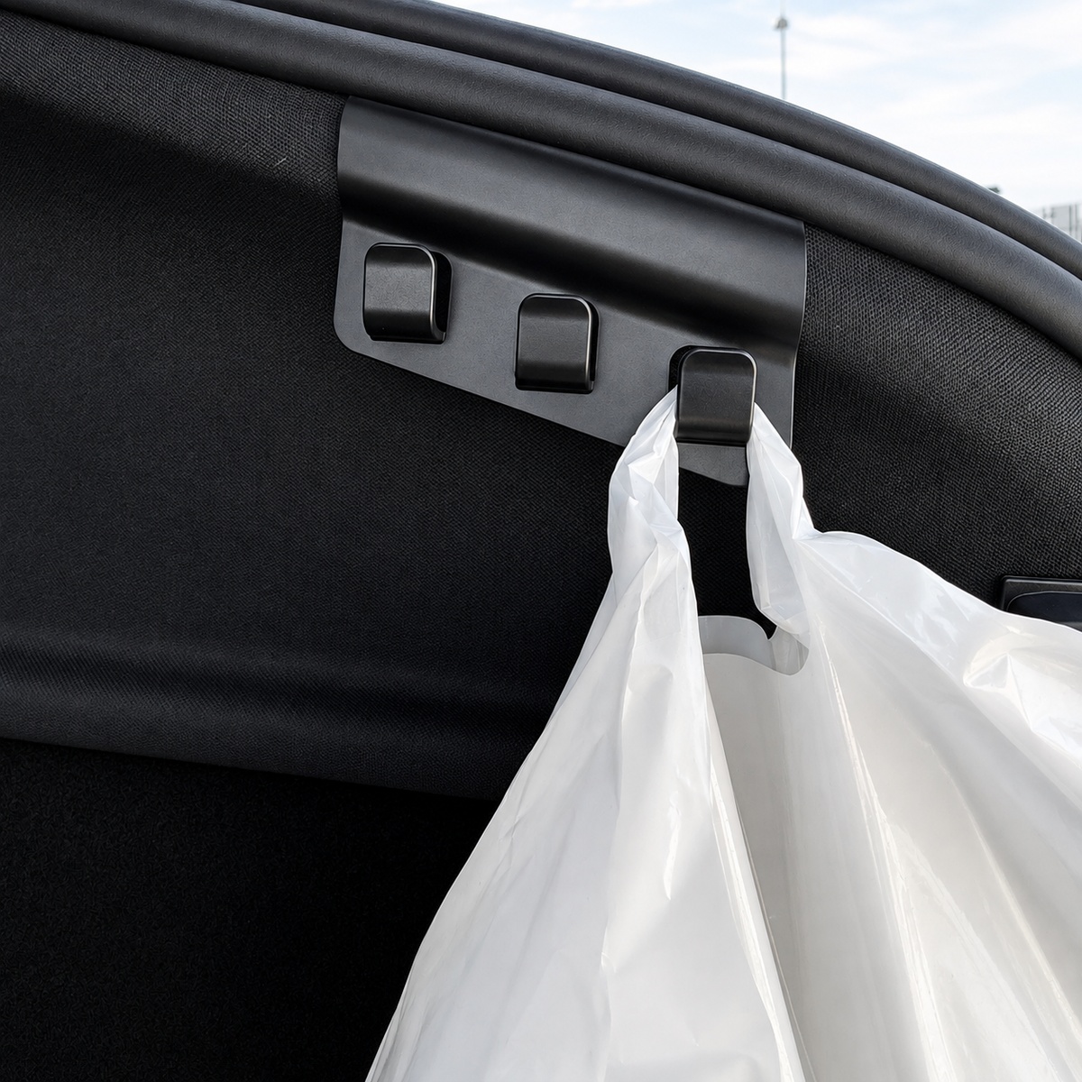 Nærbillede af bagagerumskrog med tre kroge i sort plast, hvor en pose hænger på – Tesla Model Y 2025