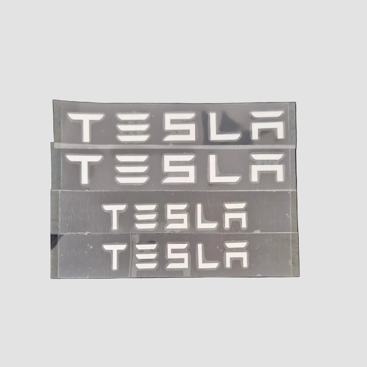 Fire sæt TESLA bogstav-emblemer i forskellige størrelser på lys baggrund
