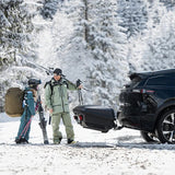 Familie med ski ved Thule Arcos XL bagageboks 450L på anhængertrækket af en sort bil i sne